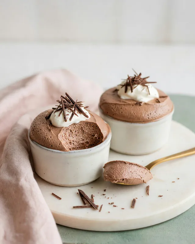 Dos pocillos de mousse de chocolate amargo con crema y virutas de chocolate.